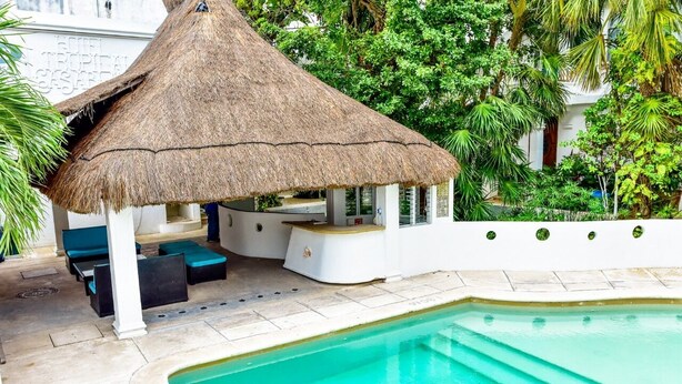 A pool area with a thatched-roof structure, lounge seating, and a pool. - Hotel tropical casa blanca  (Playa del Carmen)