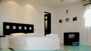 A hotel room with a bed, a black headboard, a small table, and a wall-mounted air conditioning unit. - Hotel tropical casa blanca  (Playa del Carmen)