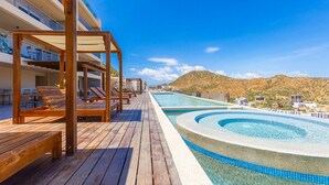 Terraza de madera con sillones de descanso y zona de piscina, con vistas a un paisaje montañoso.