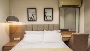 A hotel room with a bed, a nightstand, a lamp, a chair, a desk, a mirror, and two framed pictures on the wall. - Cozy 1-Bedroom in Dolphin Estate, Ikoyi with Wi-Fi, DSTV & Modern Amenities (Lagos)