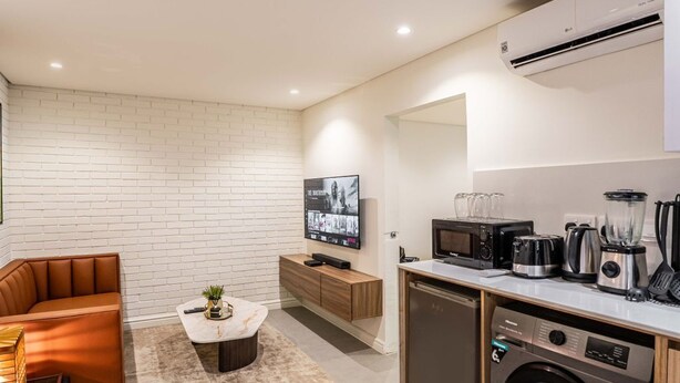 A compact living space with a sofa, a coffee table, a TV, a kitchen area with a microwave, toaster, and dishwasher. - Cozy 1-Bedroom in Dolphin Estate, Ikoyi with Wi-Fi, DSTV & Modern Amenities (Lagos)