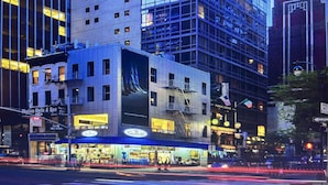 Un edificio de varios pisos con un llamativo anuncio digital, locales comerciales y una calle concurrida con semáforos.