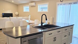 A modern kitchen with a built-in dishwasher, a black faucet, and a stainless steel sink. There are white cabinets with black handles, a round white vase on the counter, and a small table with chairs.