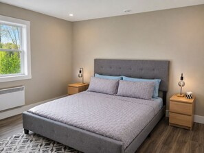 Une chambre avec un grand lit, deux tables de chevet, une fenêtre et un radiateur.