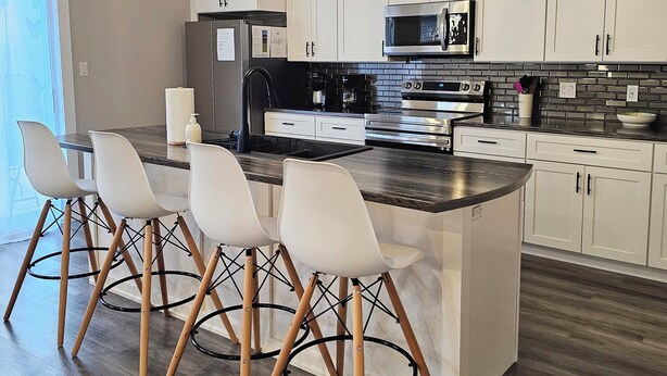 A modern kitchen with white cabinets, a central island, and bar-style chairs.