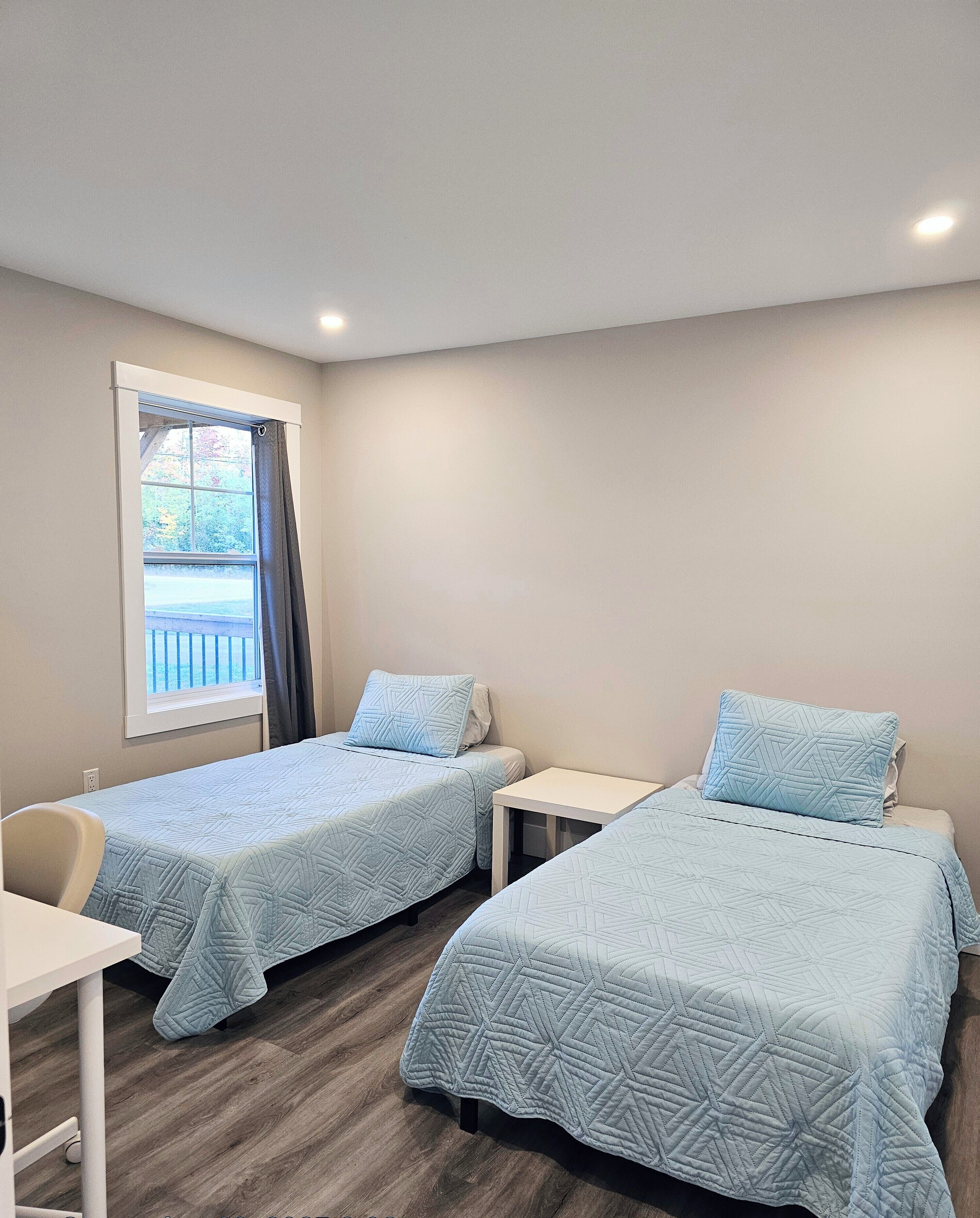Une chambre avec deux lits simples, une petite table et une fenêtre donnant sur des arbres.