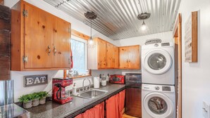 Una cocina compacta con armarios de madera, lavadora, cafetera y un lavabo.