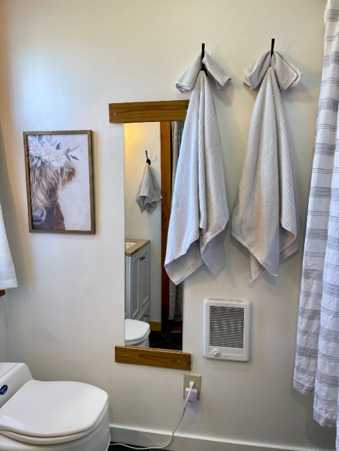 Et badeværelse med toilet, et spejl og håndklæder på en hylde.