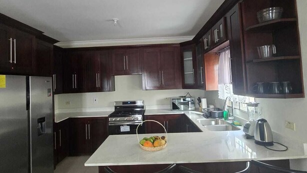 A modern kitchen with dark wood cabinets, stainless steel appliances, a central island with stools, and a checkered floor mat.