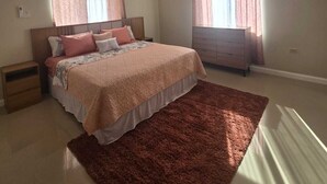 A bedroom with a bed, nightstands, a dresser, and a window with curtains.