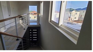 A narrow stairwell with a metal railing and a view of a residential area outside.