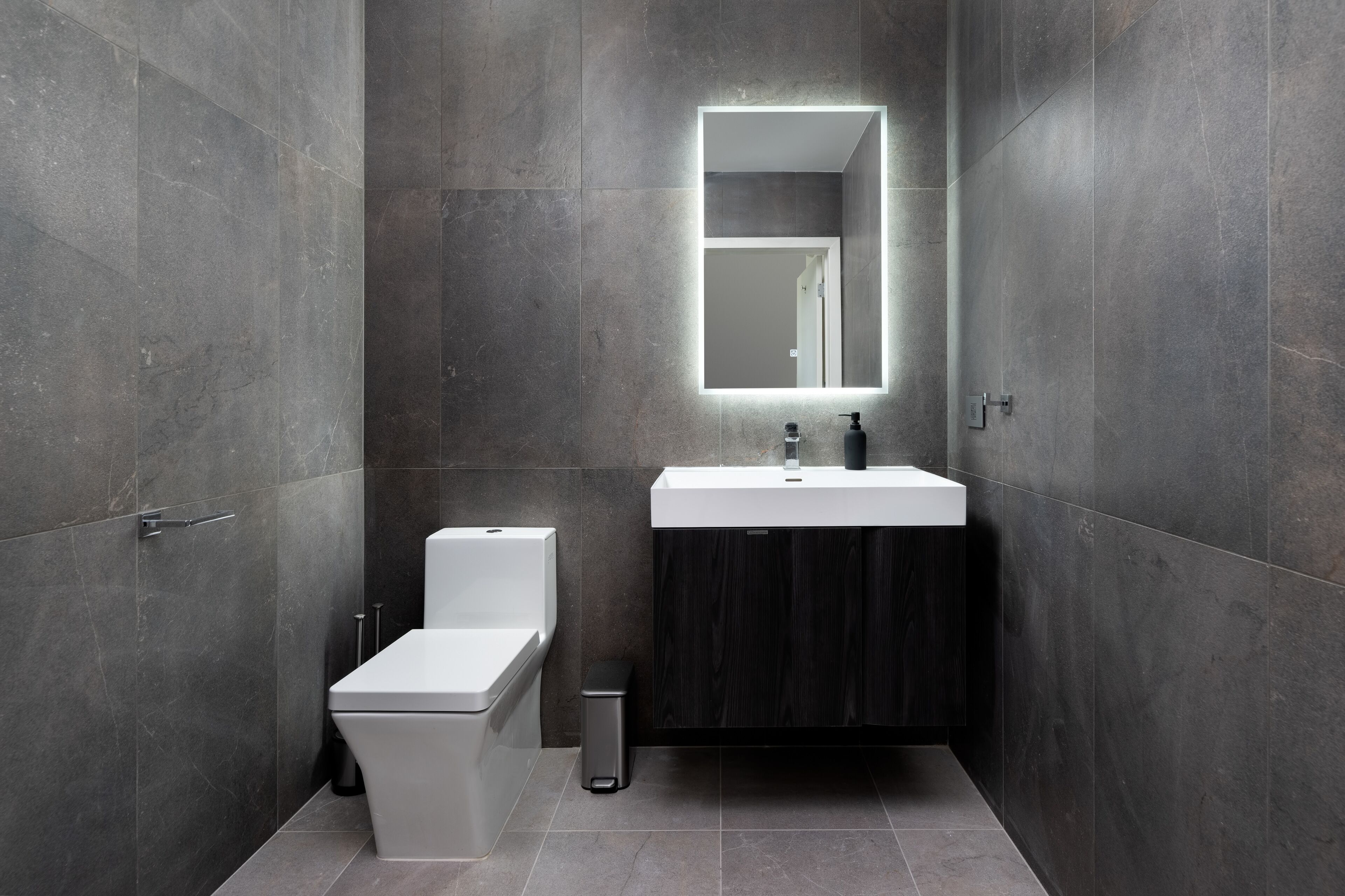 A modern bathroom with a white toilet, a sink with a mirror, and dark-toned walls.