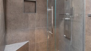 A modern shower enclosure with a glass door, a built-in bench, and a showerhead.