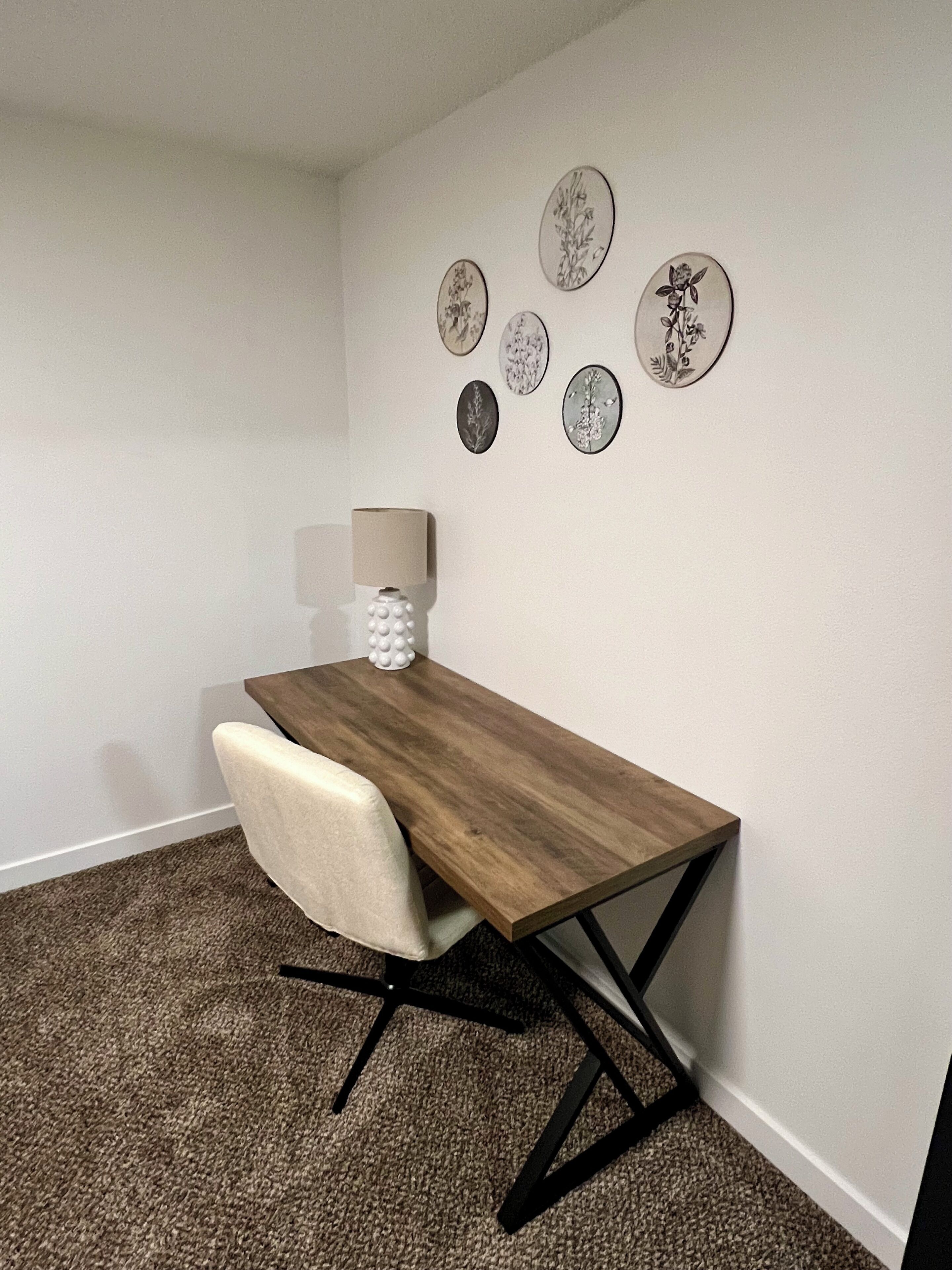 Un salón de conferencias con una mesa de madera, una silla blanca, una lámpara y decoración floral en la pared.