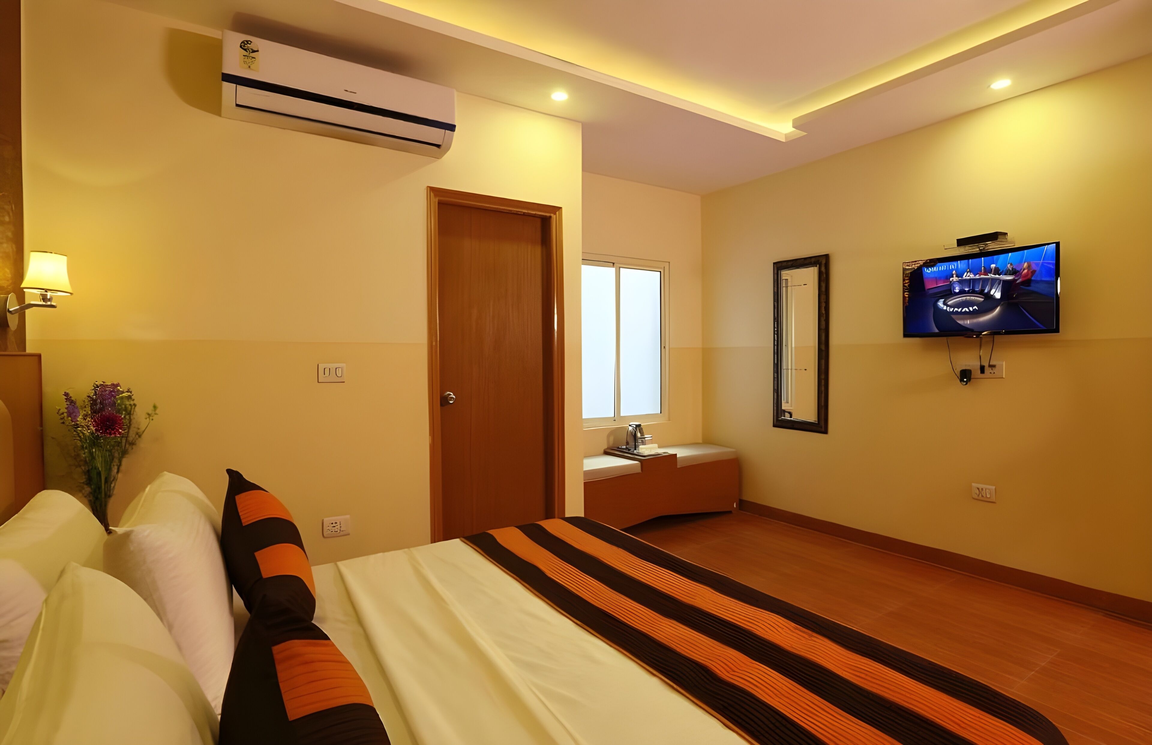 A hotel room with a bed, a TV, an air conditioner, and a window.