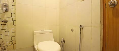A small, clean bathroom with a toilet, a shower, and a wooden door.
