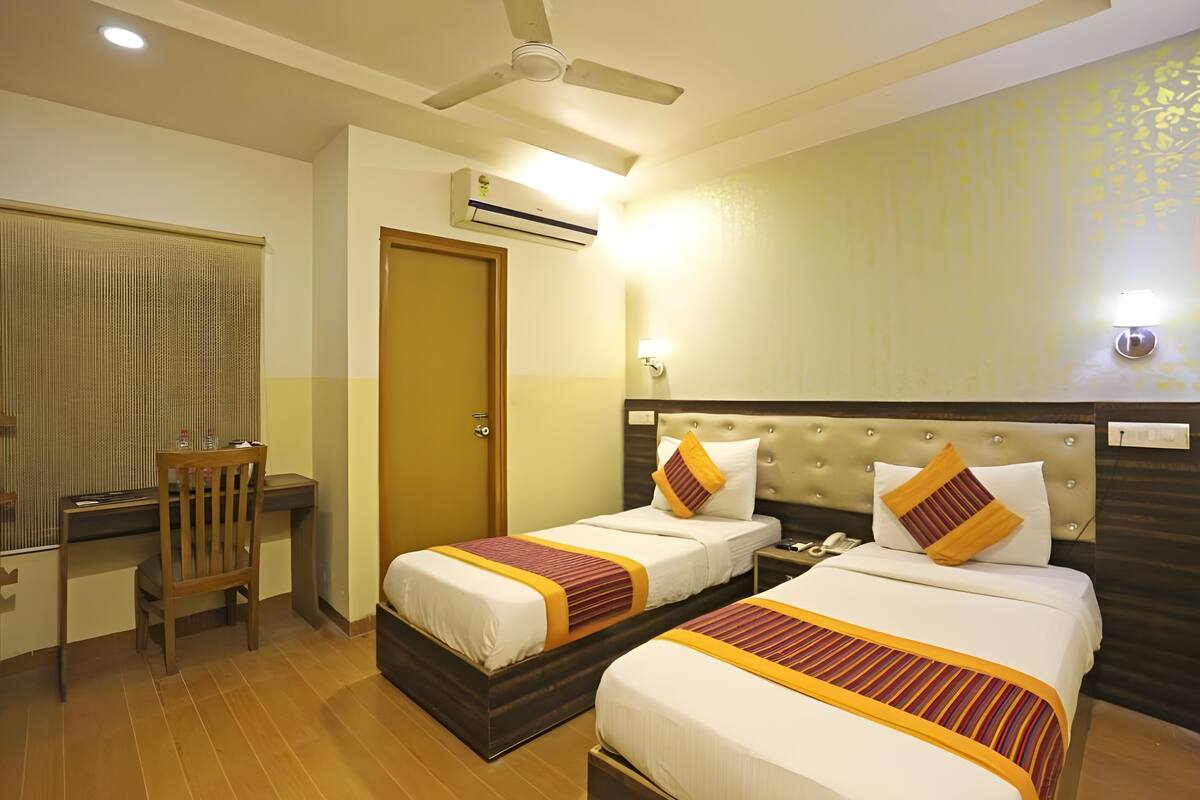 A hotel room with two beds, a desk, a chair, a ceiling fan, and an air conditioning unit.
