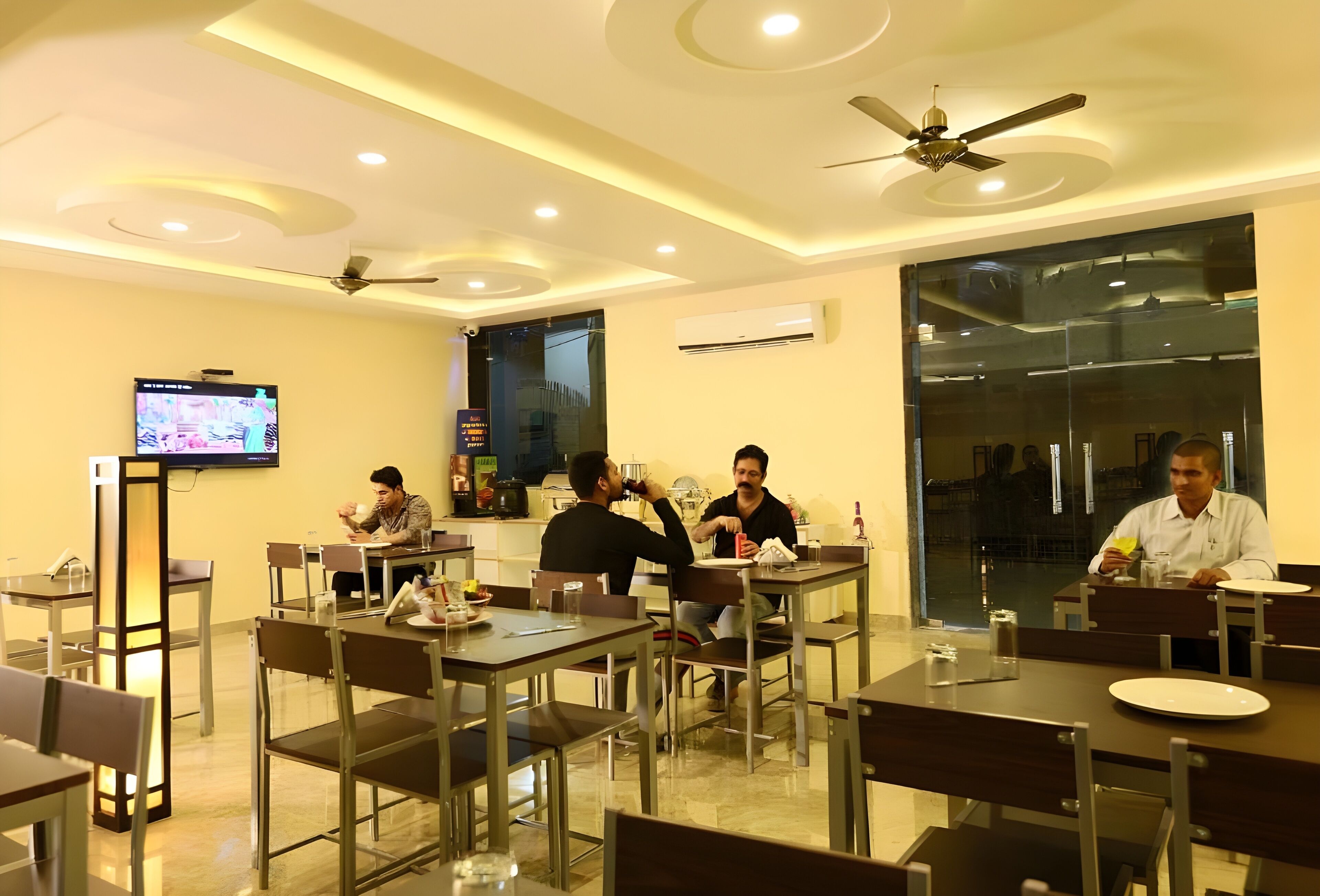 A dining area with tables, chairs, ceiling fans, and a television screen.