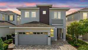 A modern two-story house with a garage, a prominent dark vertical feature on the facade, and a driveway leading to the garage.