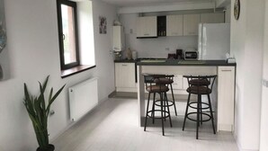 A modern kitchen with white cabinets, a central island with stools, a window, and a radiator.