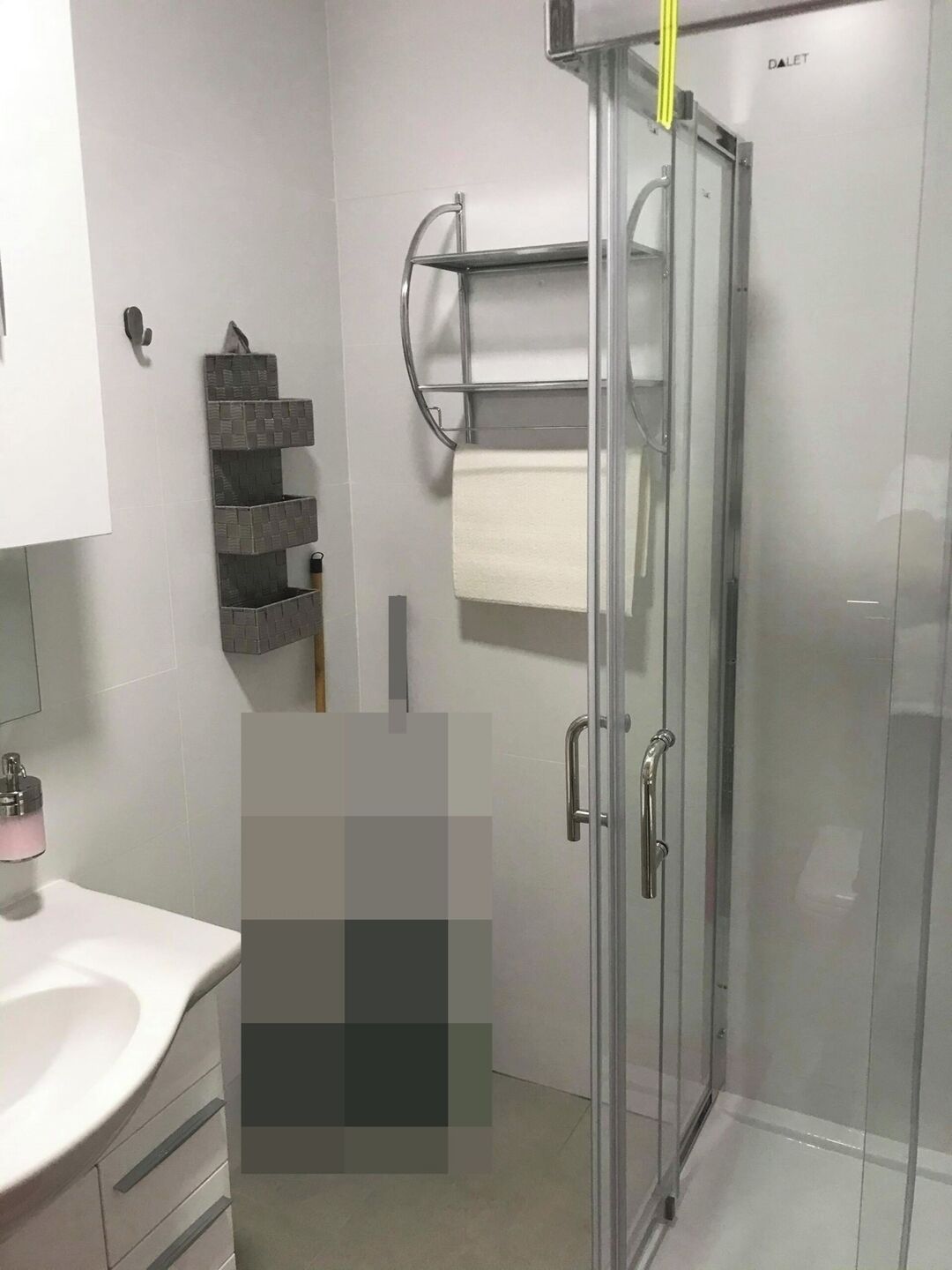 A modern bathroom with a glass shower enclosure, a white sink, and a towel rack.