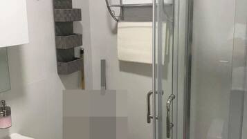 A modern bathroom with a glass shower enclosure, a white sink, and a towel rack.
