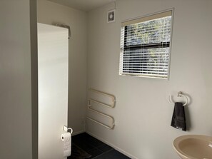 A bathroom with a toilet, a towel rack, a window with blinds, and a shower area.