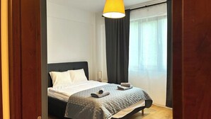 Ett modernt sovrum med en säng, ett sängbord, en lampa och ett fönster med gardiner.