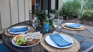 A round metal table with woven placemats, plates of food, and glasses of white wine. - Hilton Head Retreat | Gated Villa, Pets OK (Hilton Head Island)