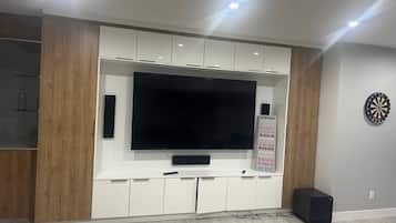 A modern living room with a large flat-screen TV mounted on a white cabinet, wooden accents, and a dartboard on the wall.