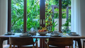 Une table à manger dressée avec des assiettes, des bols et des verres, ainsi qu’un saladier rempli de fruits et un vase de fleurs.