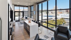 A modern kitchen with a central island, large windows offering city views, and a dining area with chairs. - Luxury 2BR 2BA Penthouse-Pool, Gym, Pkg, Views! (Salt Lake City)