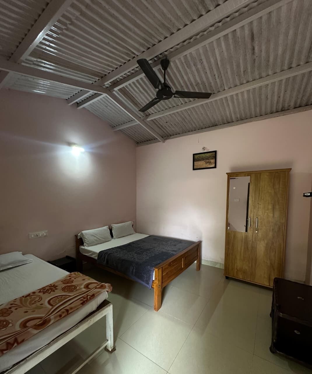 A room with a bed, a wooden wardrobe, a ceiling fan, and a door.