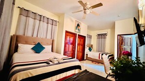 Habitación de hotel con cama, escritorio, silla, ventilador de techo y una puerta.