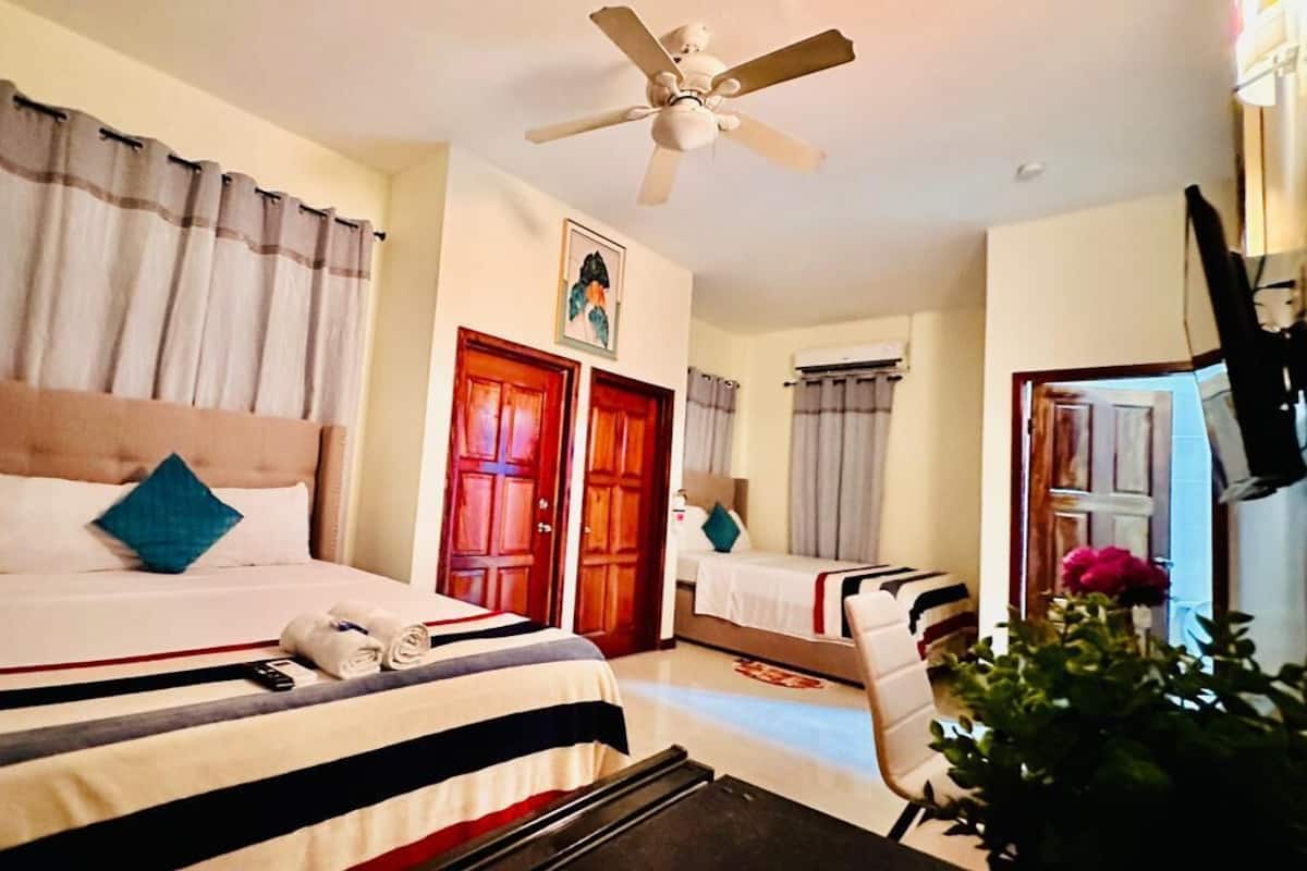 A hotel room with a bed, a desk, a chair, a ceiling fan, and a door.