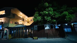 Un edificio de varios pisos con área de recepción, una zona delimitada para alquiler de carros de golf y un árbol en la fachada.