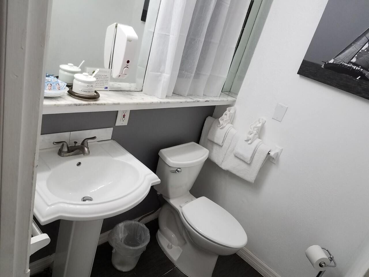 A compact bathroom with a white sink, toilet, and a small trash bin.