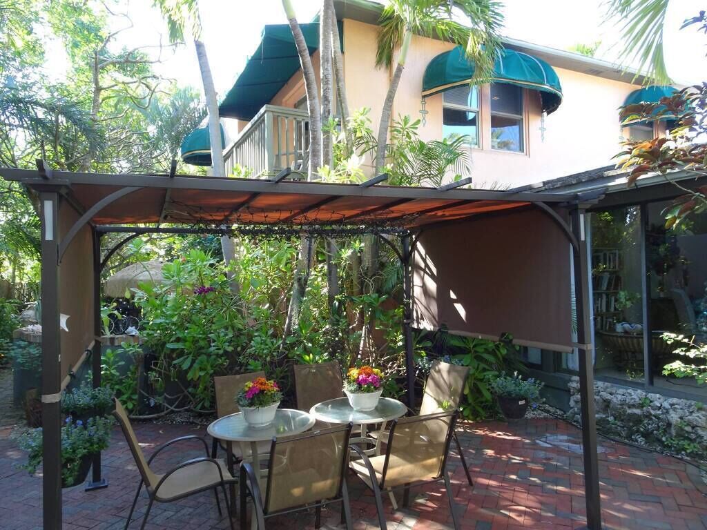 Une terrasse extérieure dotée d’un espace salon couvert, entourée d’une végétation luxuriante et bordée d’un bâtiment surmonté d’un toit végétalisé.