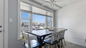 Ein Essbereich mit Tisch und Stühlen, einem Deckenventilator und Blick durch große Fenster.