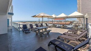 Eine Dachterrasse mit Liegestühlen, Sonnenschirmen und Blick auf den Strand.