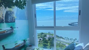 Un dormitorio con un ventanal que ofrece vistas a la costa, una cama con almohadas y una manta.