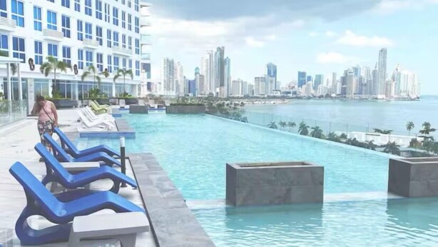 Zona de piscina con sillas de descanso y un horizonte urbano al fondo.