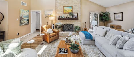 A spacious living room with a high ceiling, a stone fireplace, and a variety of seating options including a leather armchair and a sofa.