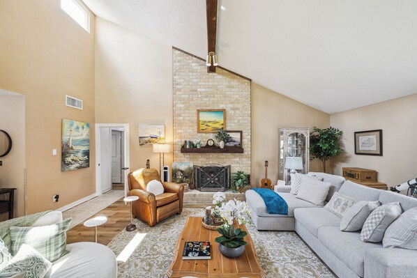 A spacious living room with a high ceiling, a stone fireplace, and a variety of seating options including a leather armchair and a sofa.