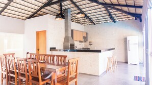 Une cuisine spacieuse dotée d’un grand îlot central, de chaises en bois et d’un plafond haut avec des poutres apparentes.