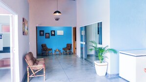 Un hall d’entrée spacieux avec un mur d’accent bleu, deux fauteuils en osier, une plante en pot et un appareil électroménager blanc, probablement un lave-linge et un sèche-linge.