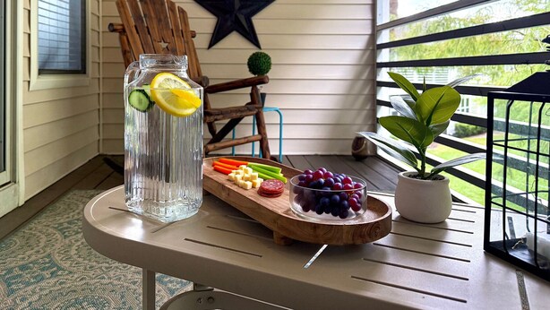 Une table avec une carafe d’eau, une planche à découper en bois sur laquelle sont disposés des fruits et des légumes, une décoration en forme d’étoile et une chaise.