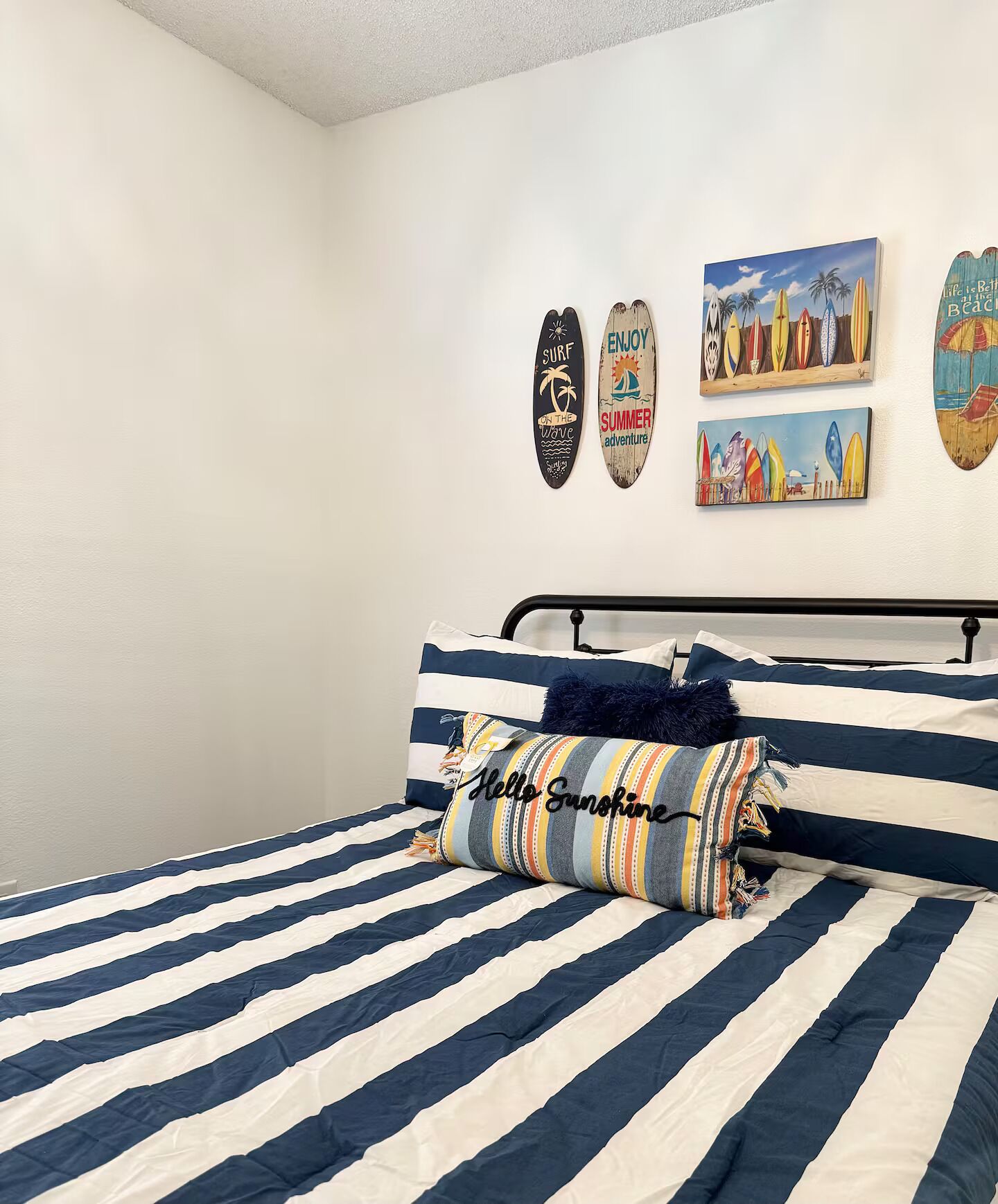 A bedroom with a bed featuring striped bedding, a metal headboard, and a pillow with a nautical theme.