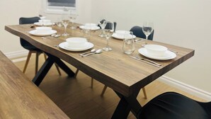 Een eettafel gedekt met witte borden, kommen en bestek, omringd door stoelen.