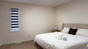 Een slaapkamer met een bed, een nachtkastje, een raam met jaloezieën en een plafondlamp.
